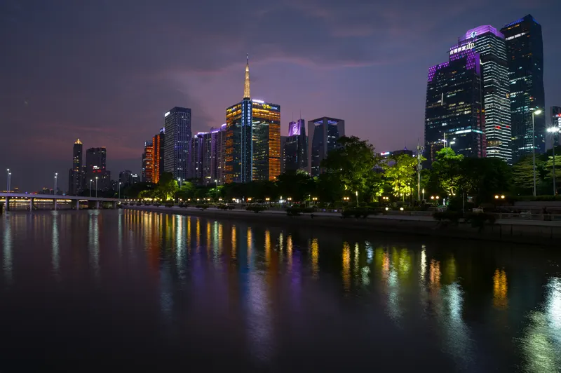 城市夜景，隔江望去，摩天楼的霓虹与岸边的一起倒映在水面上，紫橙色的光带交叠